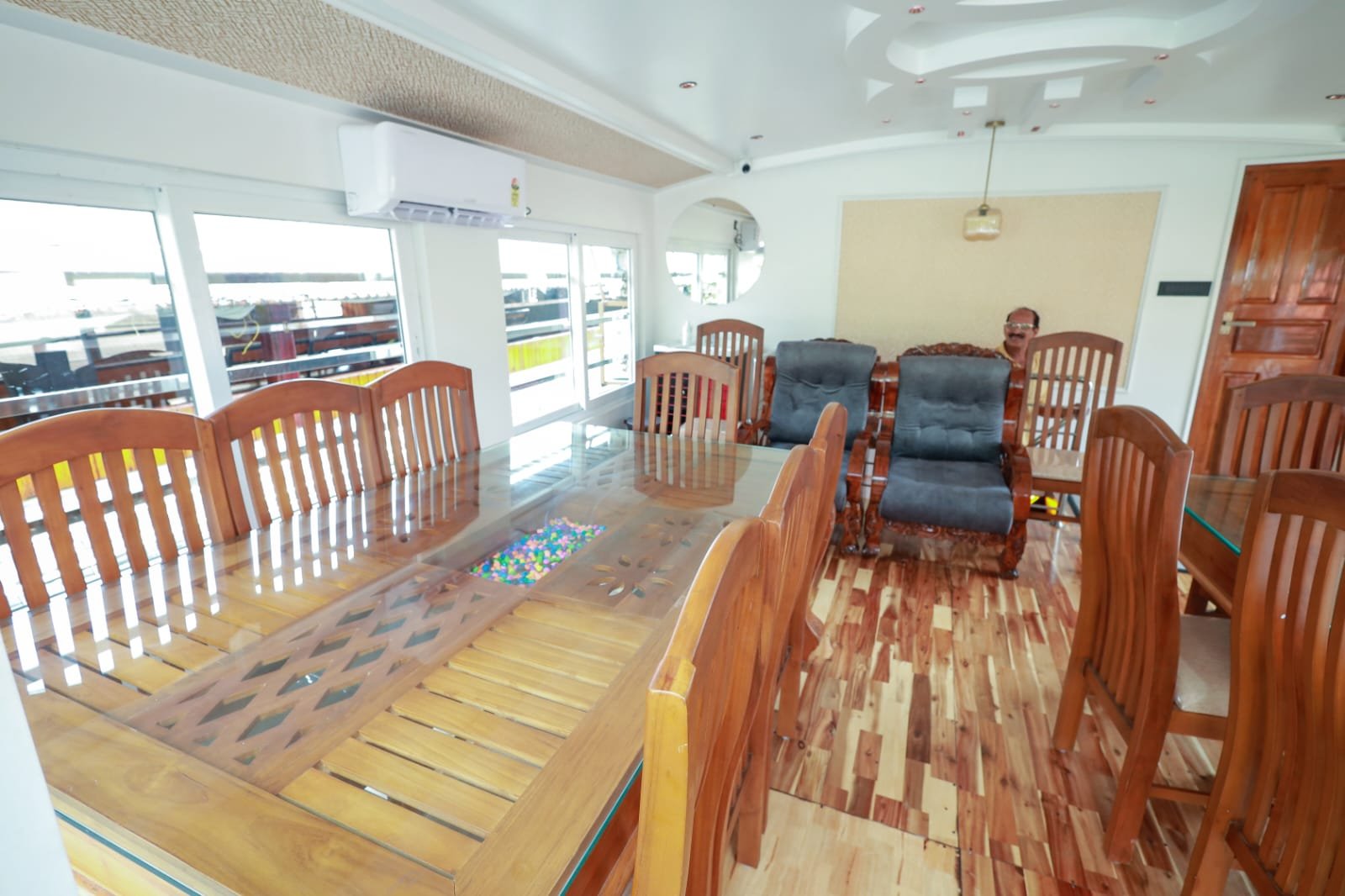 Large air-conditioned dining area with a glass-topped wooden table inside a 5 bedroom houseboat Alleppey.