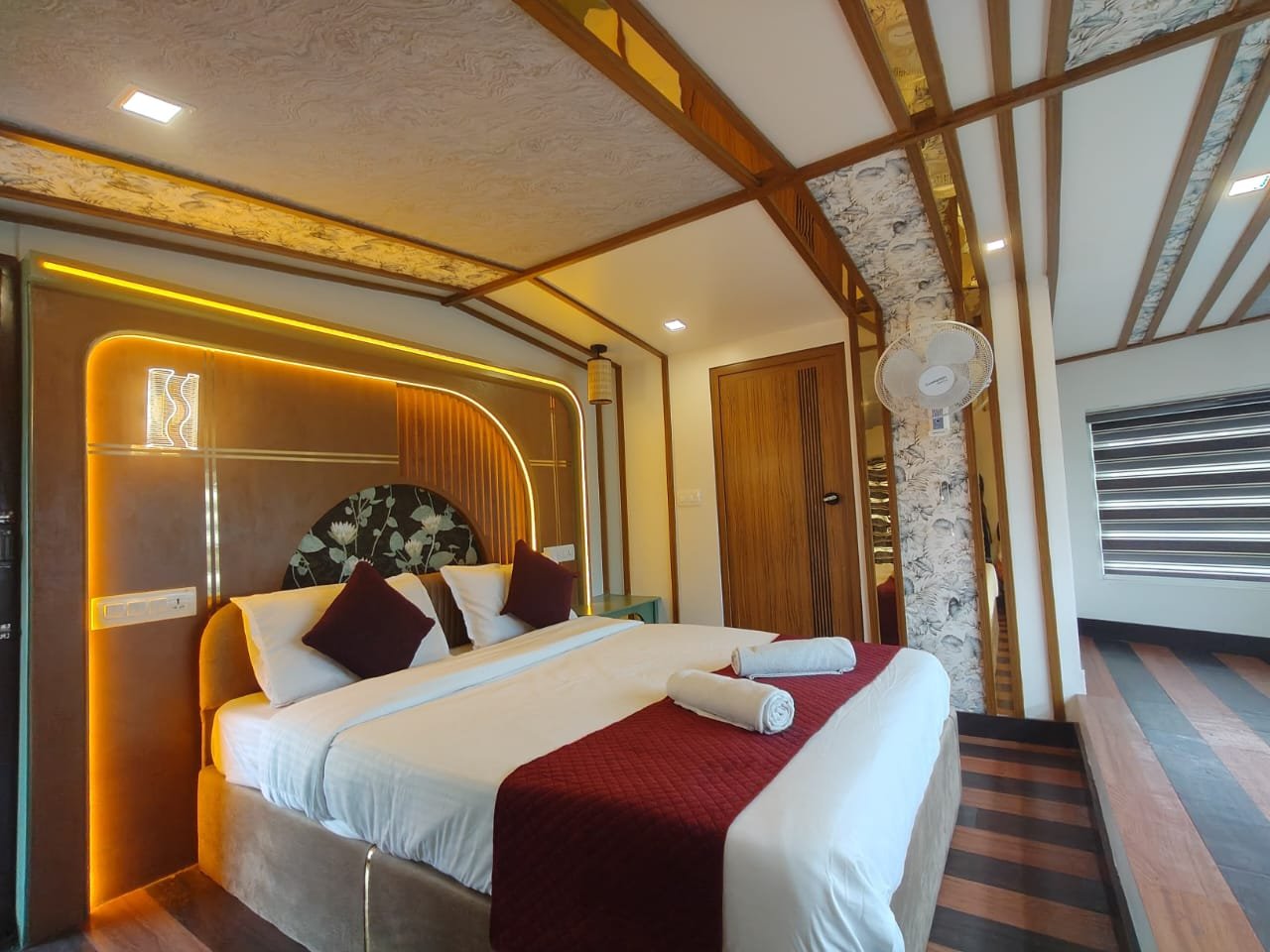 Premium Modern Bedroom - 6 Bedroom Houseboat Alleppey Premium modern bedroom with stylish LED headboard, large scenic windows, and striped flooring on a 6 bedroom houseboat alleppey.
