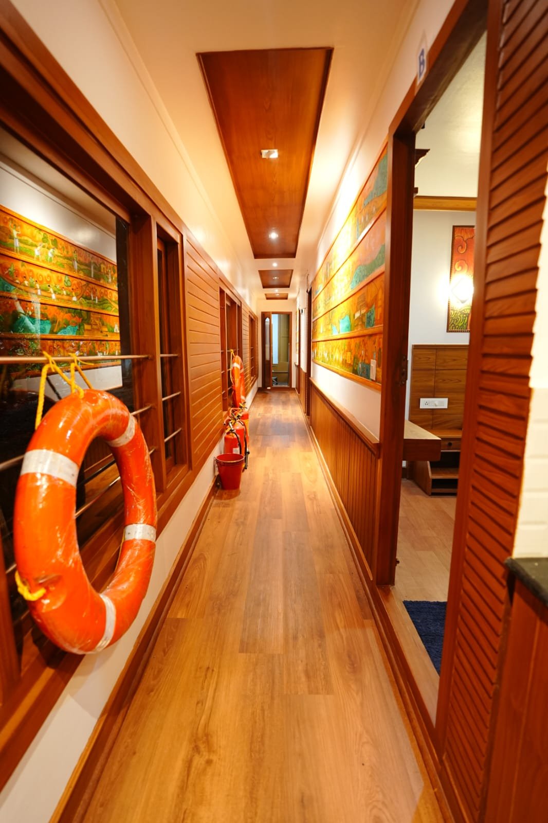 Elegant wooden hallway adorned with traditional Kerala murals connecting the rooms of the houseboat.