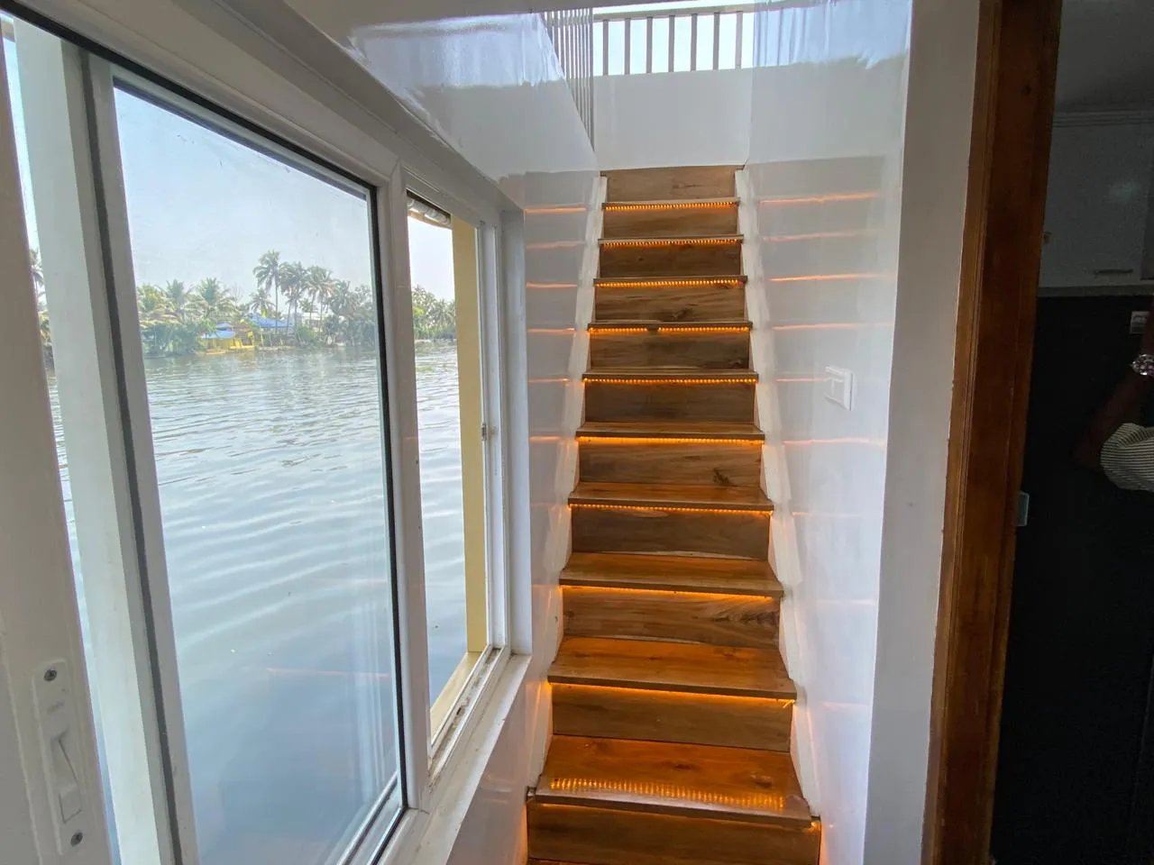 Illuminated wooden staircase leading to the upper deck of the 10 bedroom houseboat alleppey